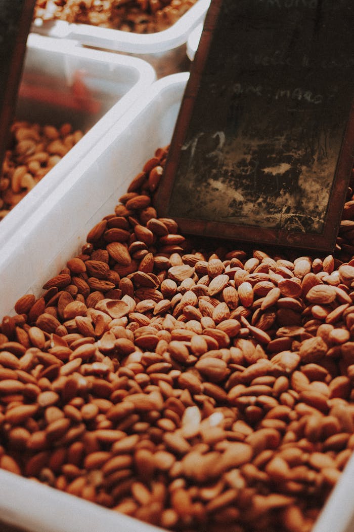 From above of heap of tasty almond nuts placed in plastic containers with wooden scoop on local bazaar